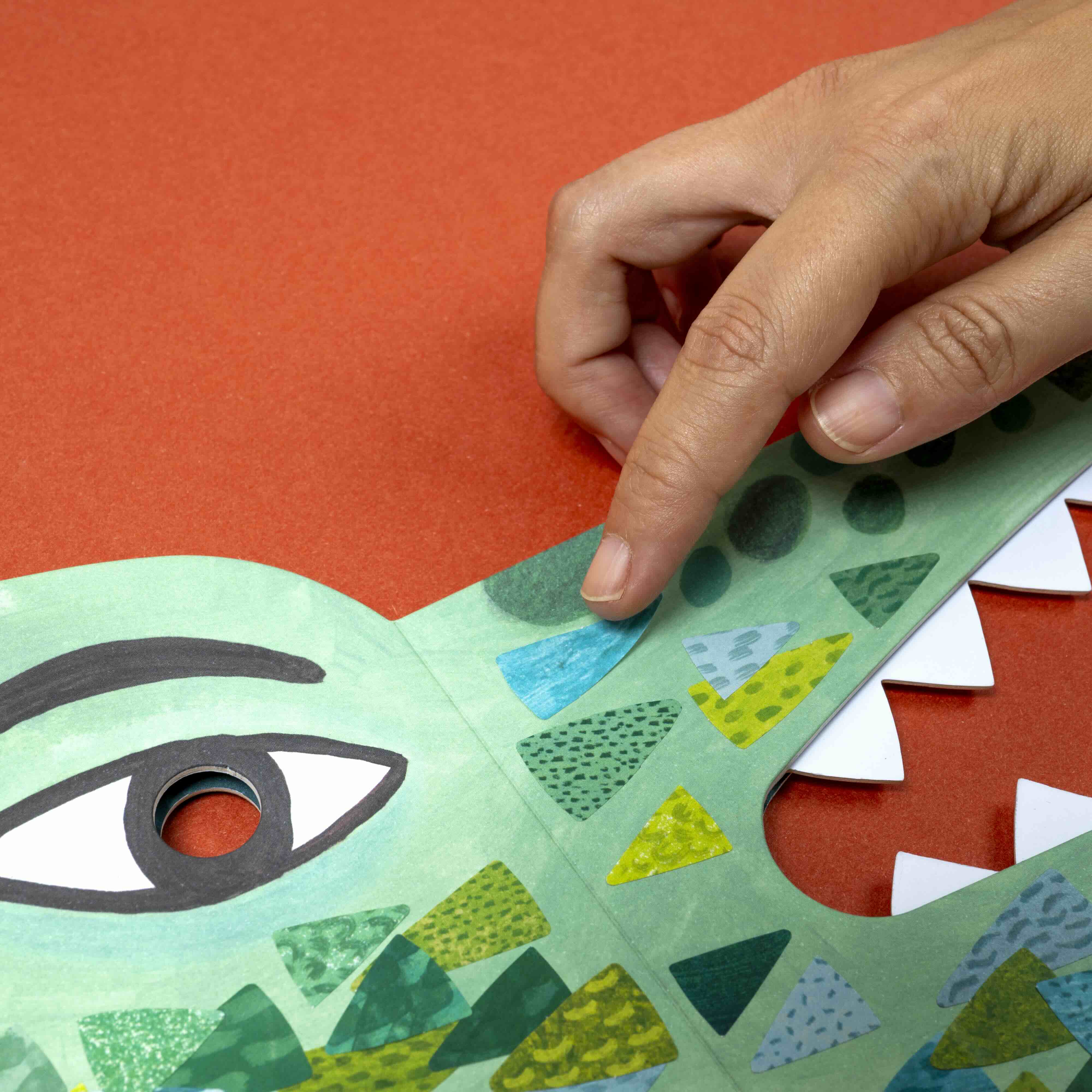 Hand interacting with a colorful paper crocodile mask on an orange background