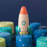 Londji wooden toy rocket among colorful cylindrical blocks with star patterns on a dark blue background