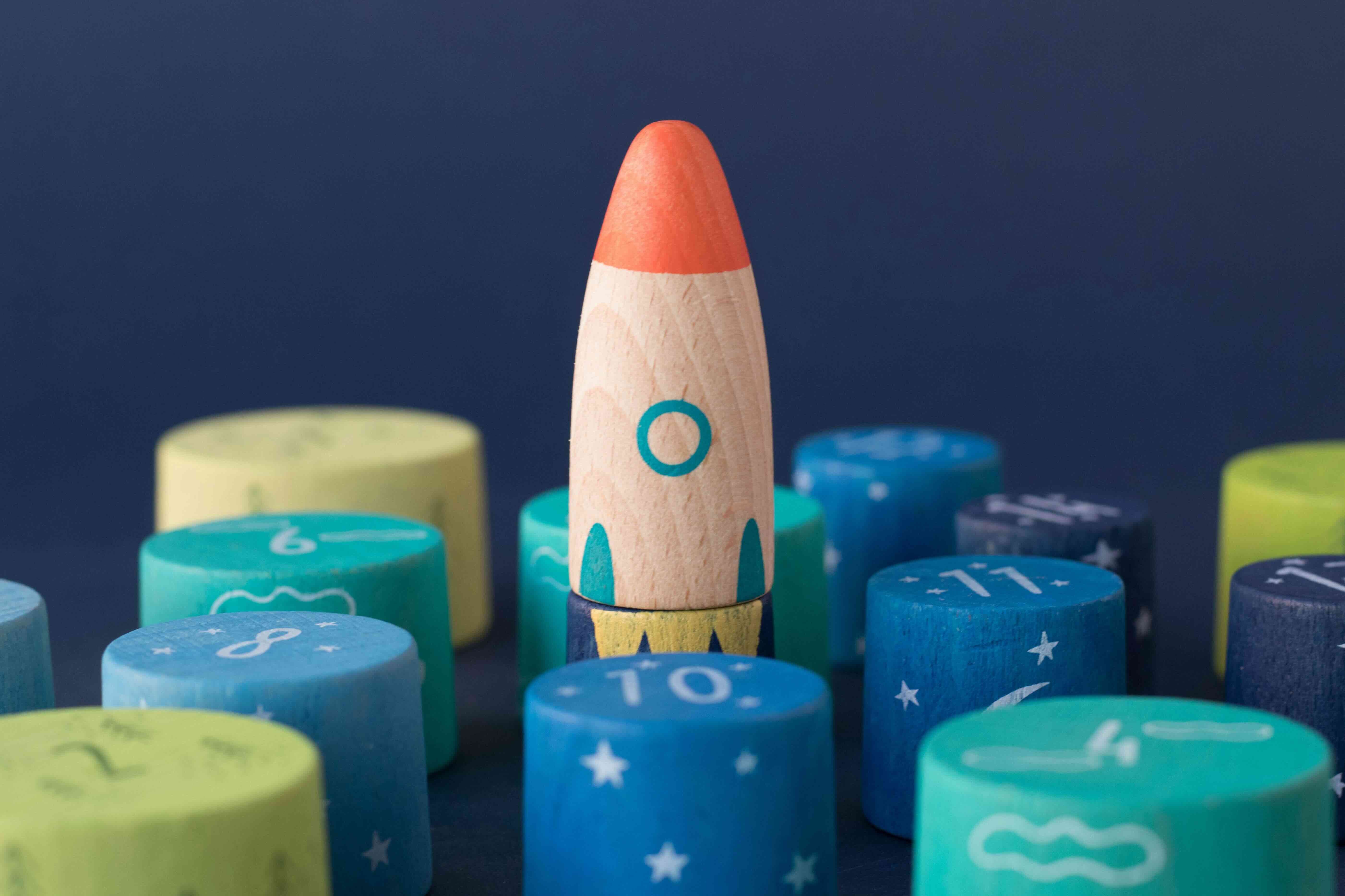 Londji wooden toy rocket among colorful cylindrical blocks with star patterns on a dark blue background