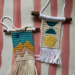 Two small woven wall hangings with colorful patterns on a striped fabric background.