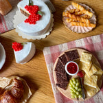 Assorted desserts including a cake with red berries, cookies, and fruit on a wooden table.