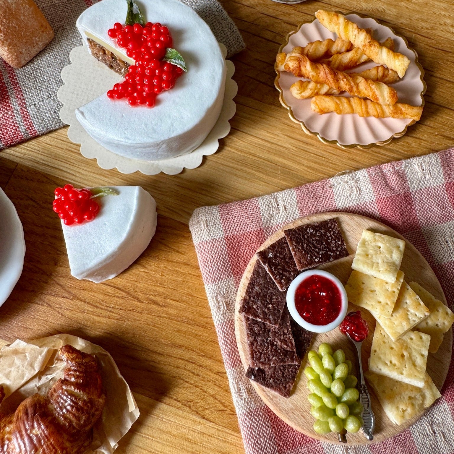 Assorted desserts including a cake with red berries, cookies, and fruit on a wooden table.