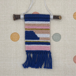 Small woven wall hanging with colorful pattern on a textured surface