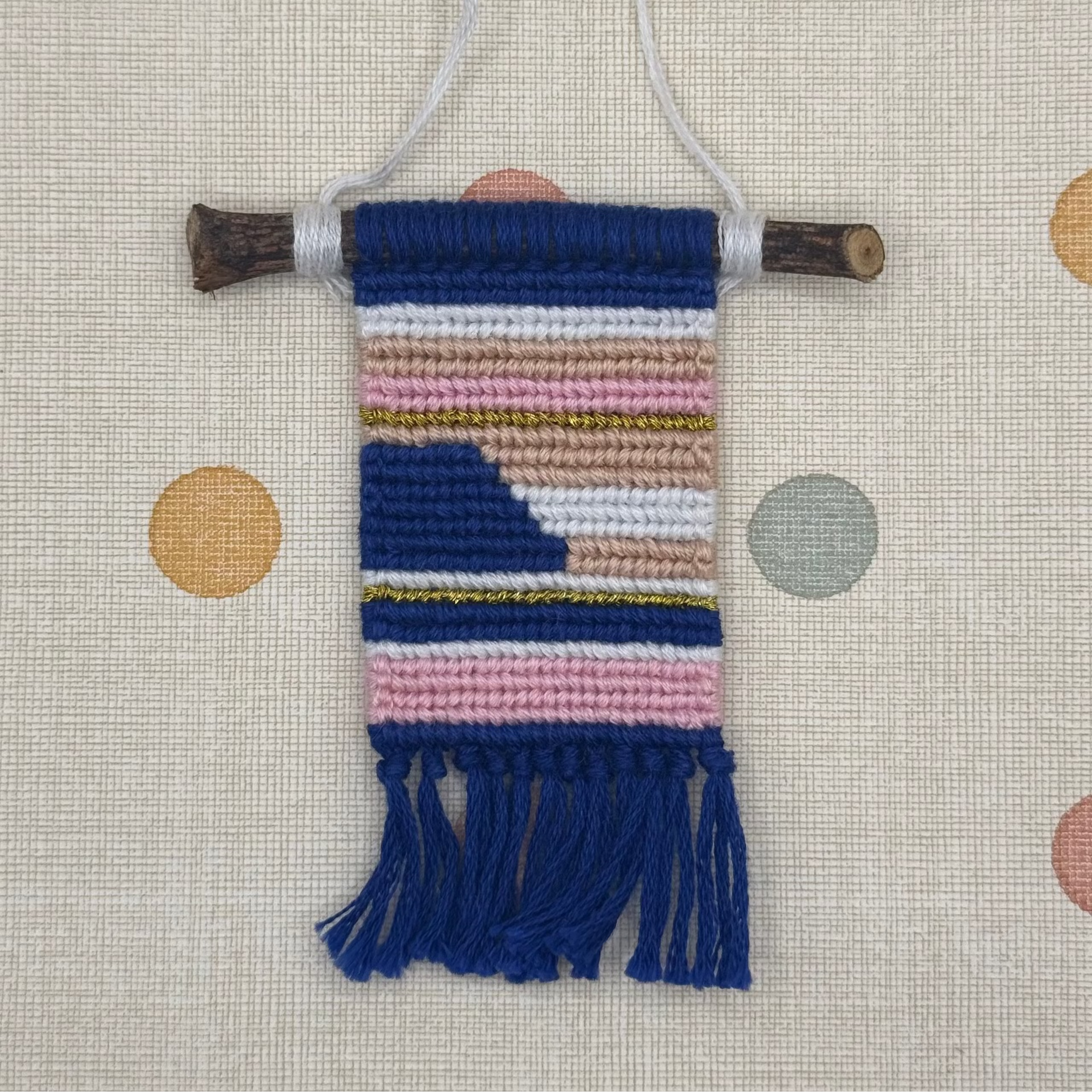 Small woven wall hanging with colorful pattern on a textured surface