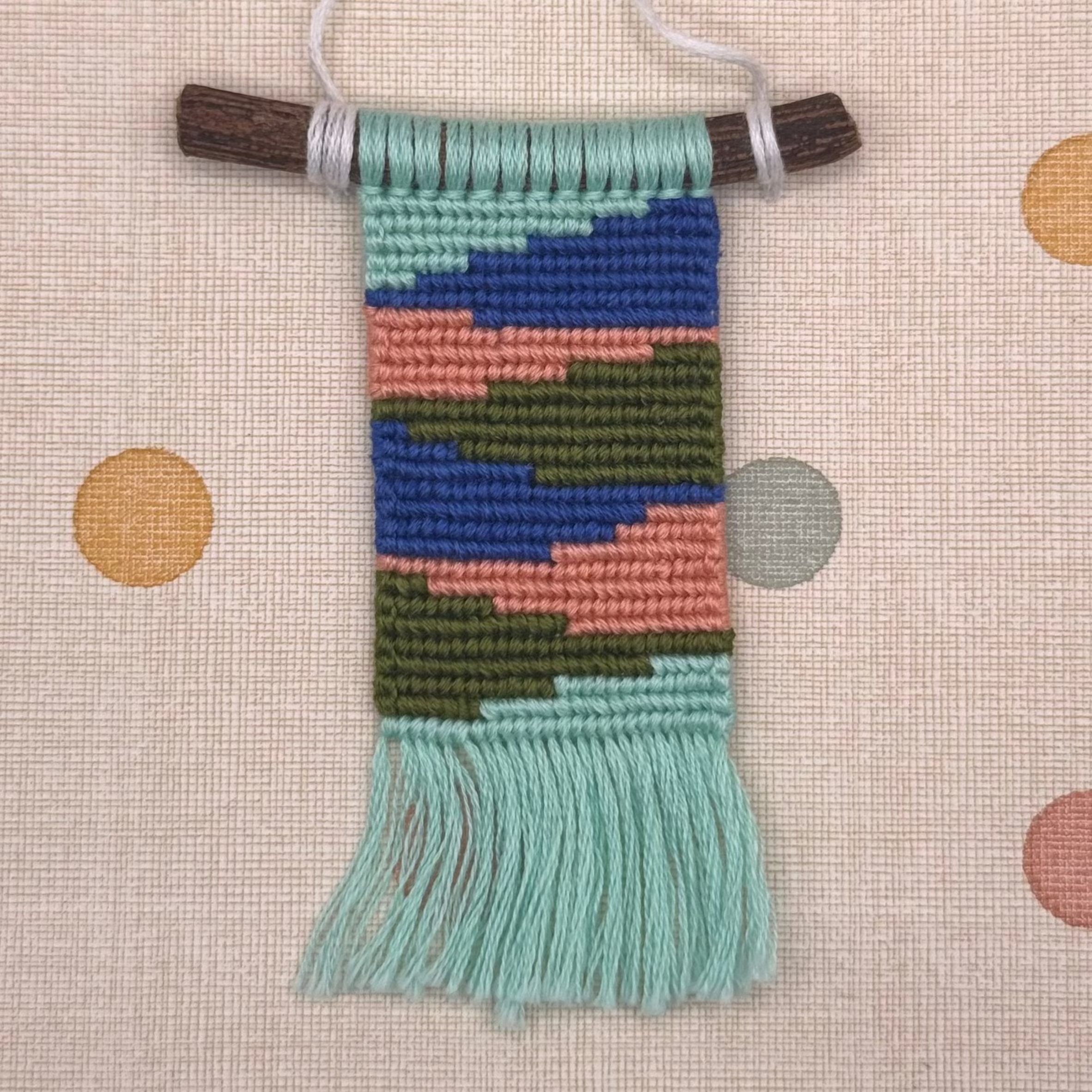 Handmade woven ornament with colorful pattern on a polka dot background