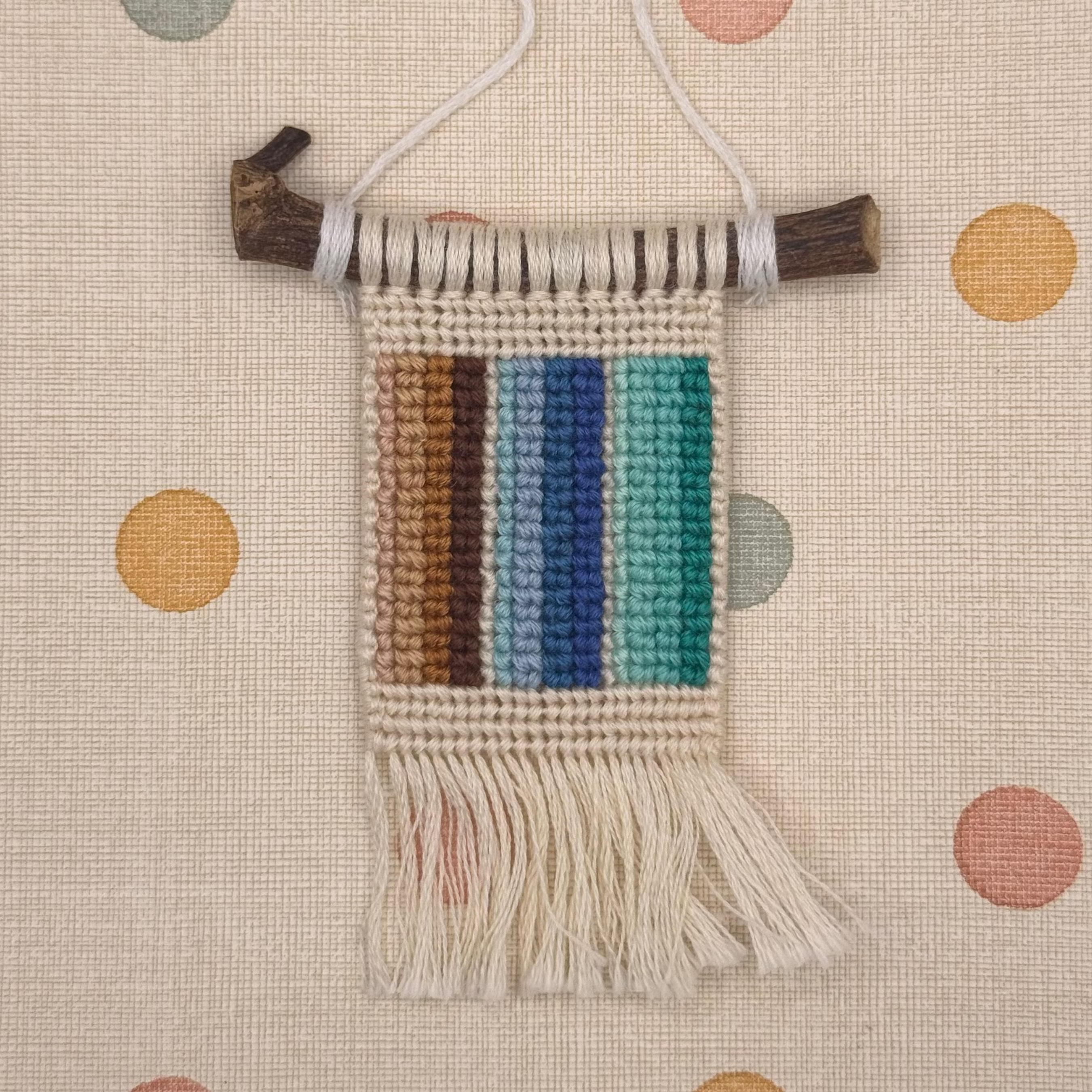 Woven wall hanging with colorful stripes on a polka dot background