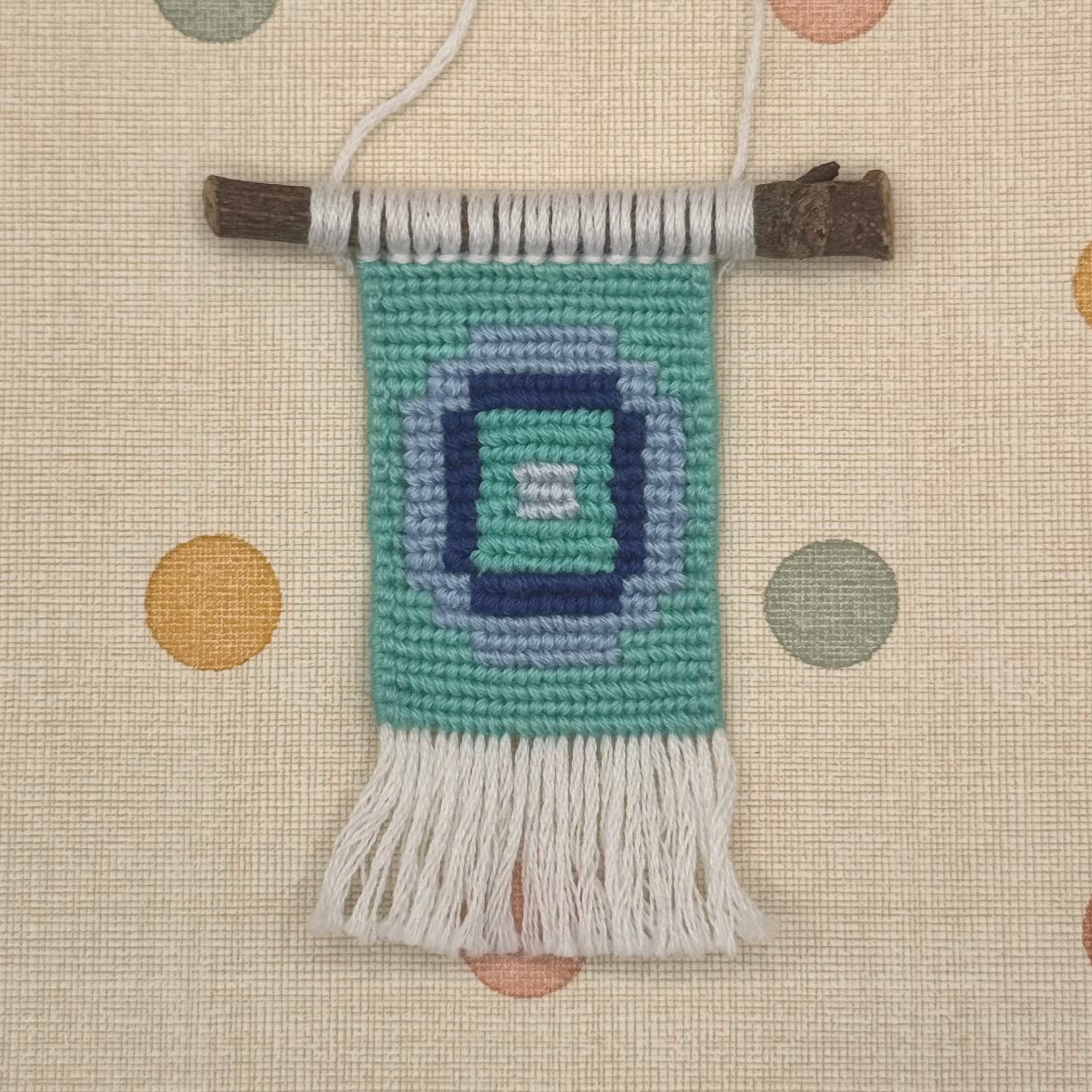 Handmade woven wall hanging with a geometric pattern on a polka dot background