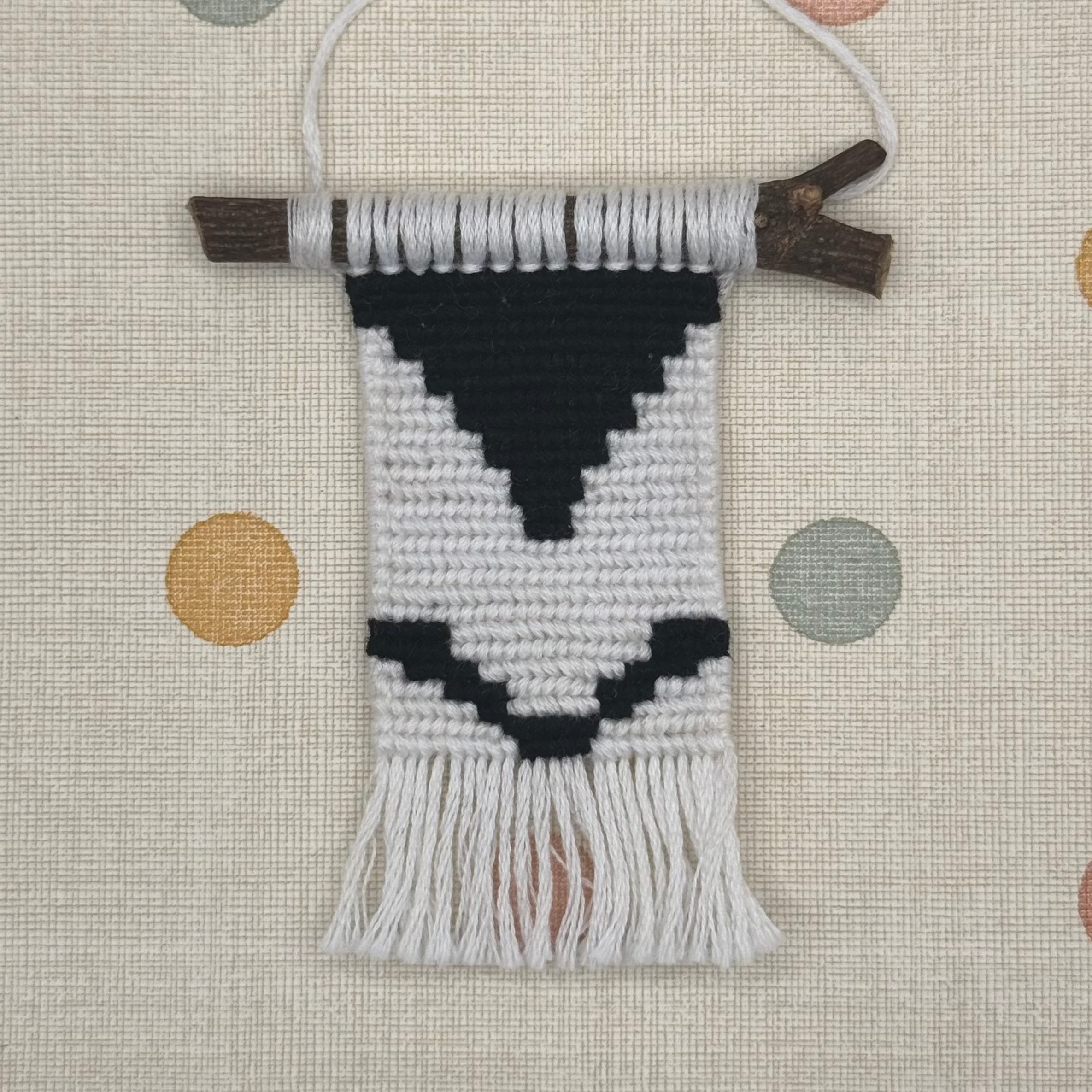 Textile art piece with black and white pattern on a polka dot background
