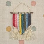 Woven wall hanging with colorful stripes and fringes on a polka dot background