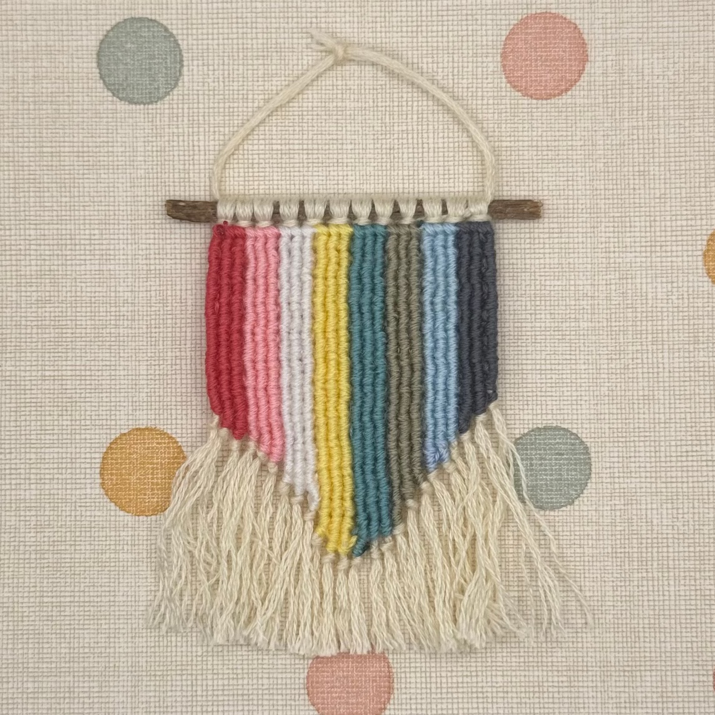 Woven wall hanging with colorful stripes and fringes on a polka dot background