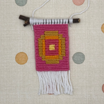 Small woven wall hanging with a colorful design on a polka dot background