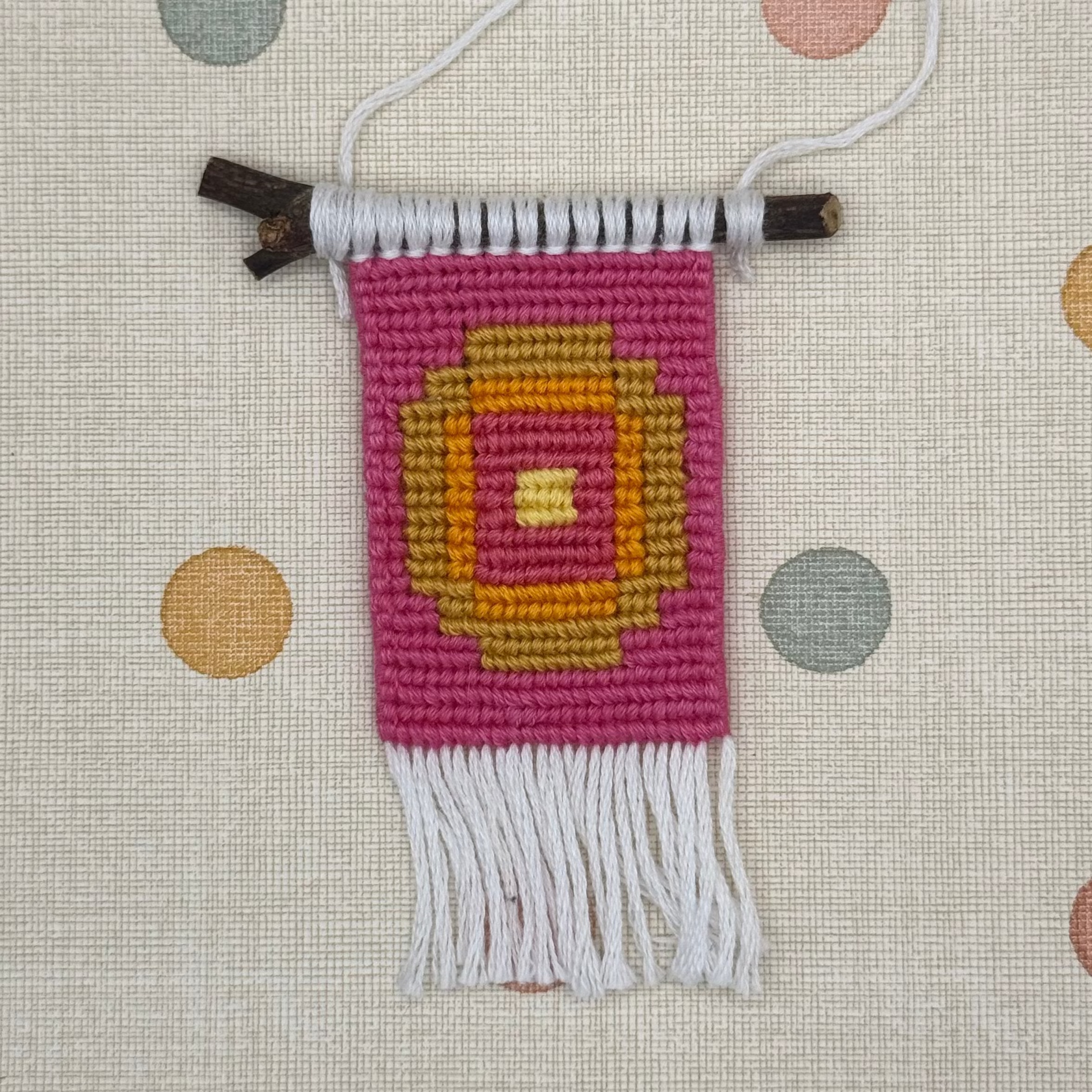 Small woven wall hanging with a colorful design on a polka dot background