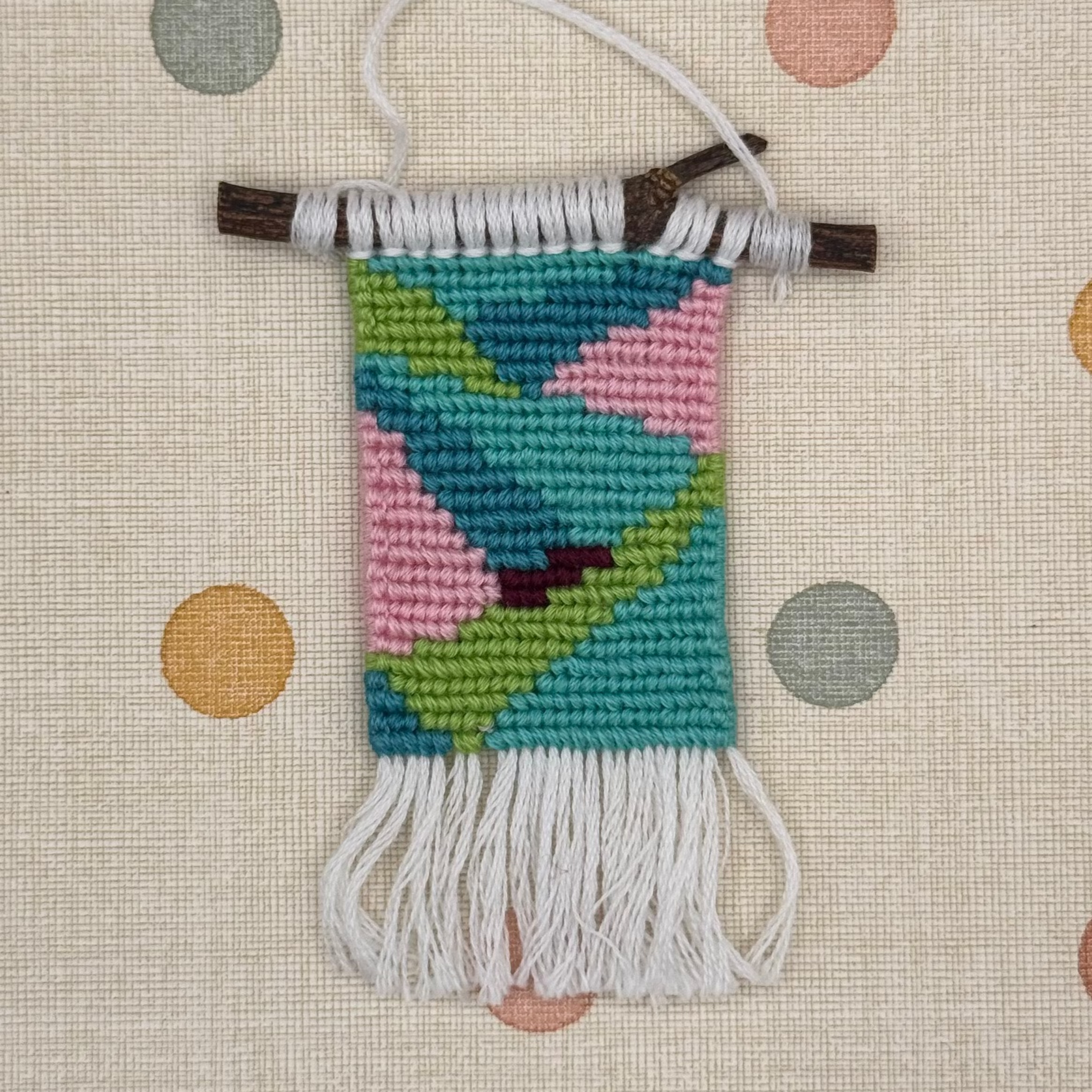 Small woven wall hanging with colorful pattern on a polka dot background