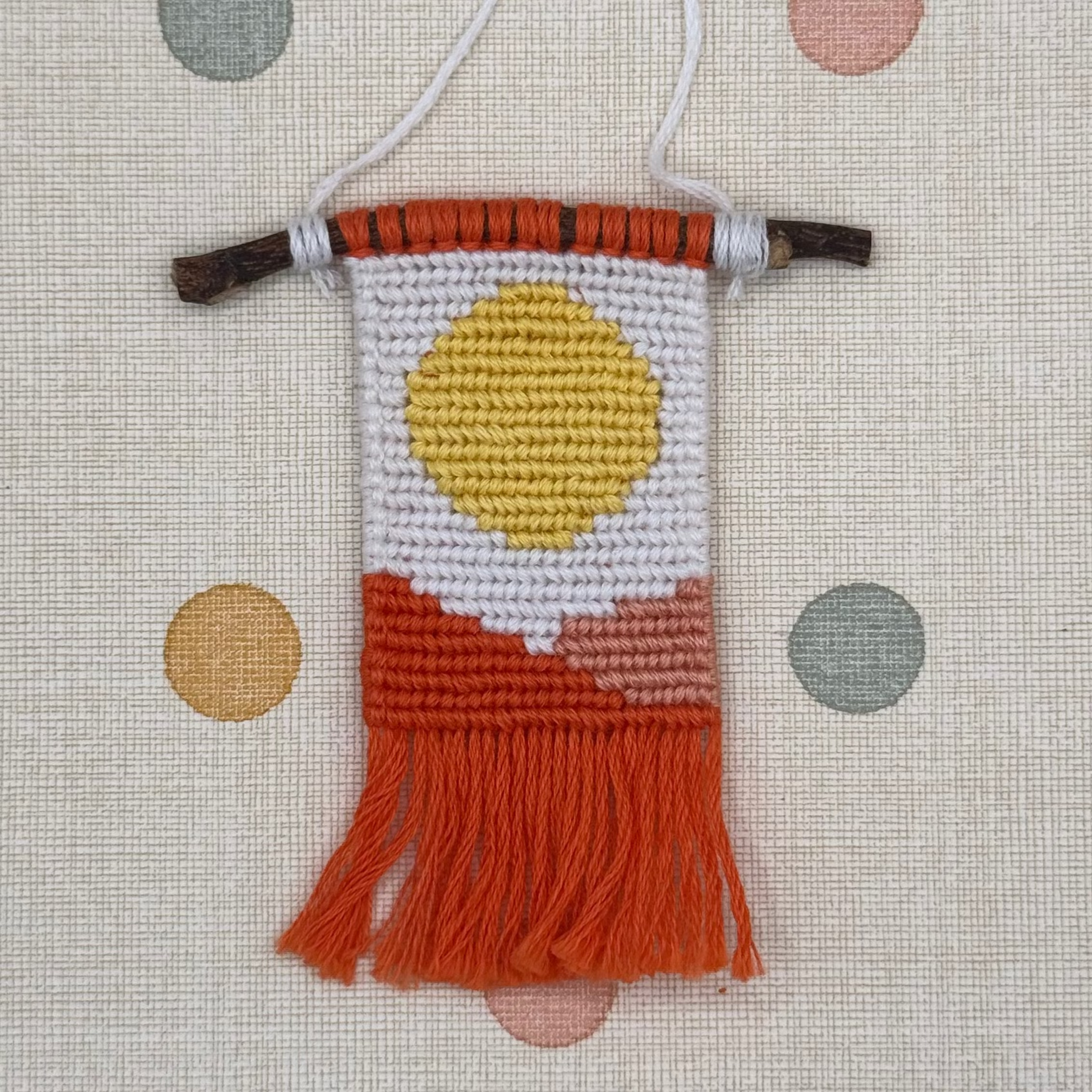 Small woven wall hanging with a sun design on a polka dot background