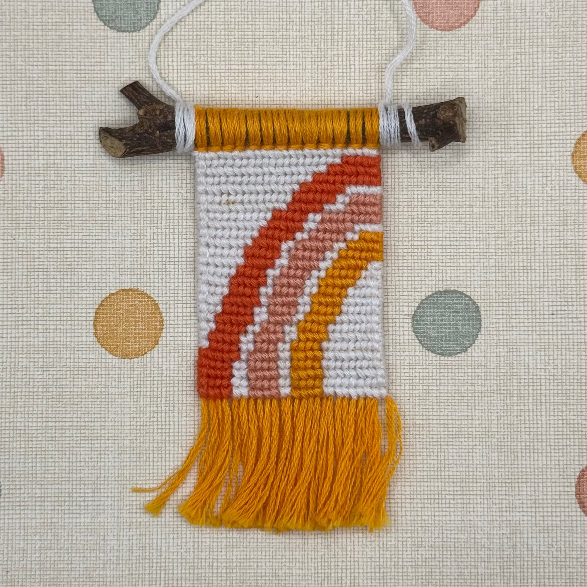 Textile art piece with colorful patterns and fringes on a textured background