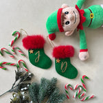 Christmas-themed items including a plush elf, stockings, candy canes, and mistletoe on a light background.