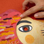 Hand interacting with a colorful paper lion mask by Londji on an orange background