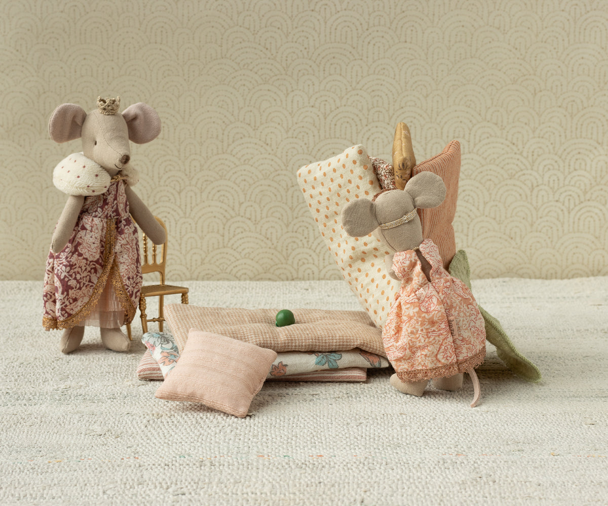 Two plush mouse toys with dresses on a textured surface and patterned wall background