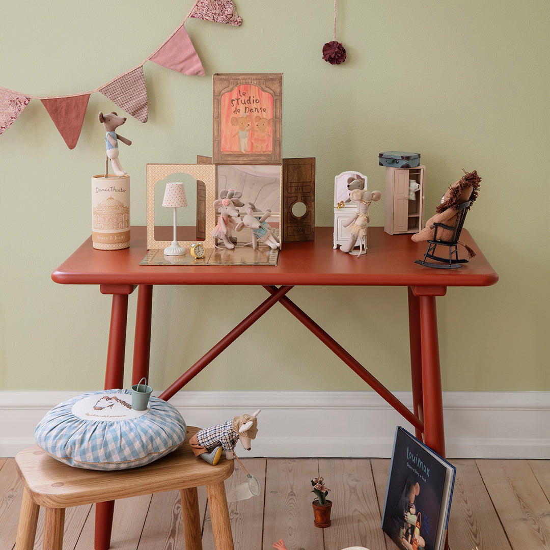 Maileg toys in a children's playroom with a red table and various toys and decorations on a wooden floor.