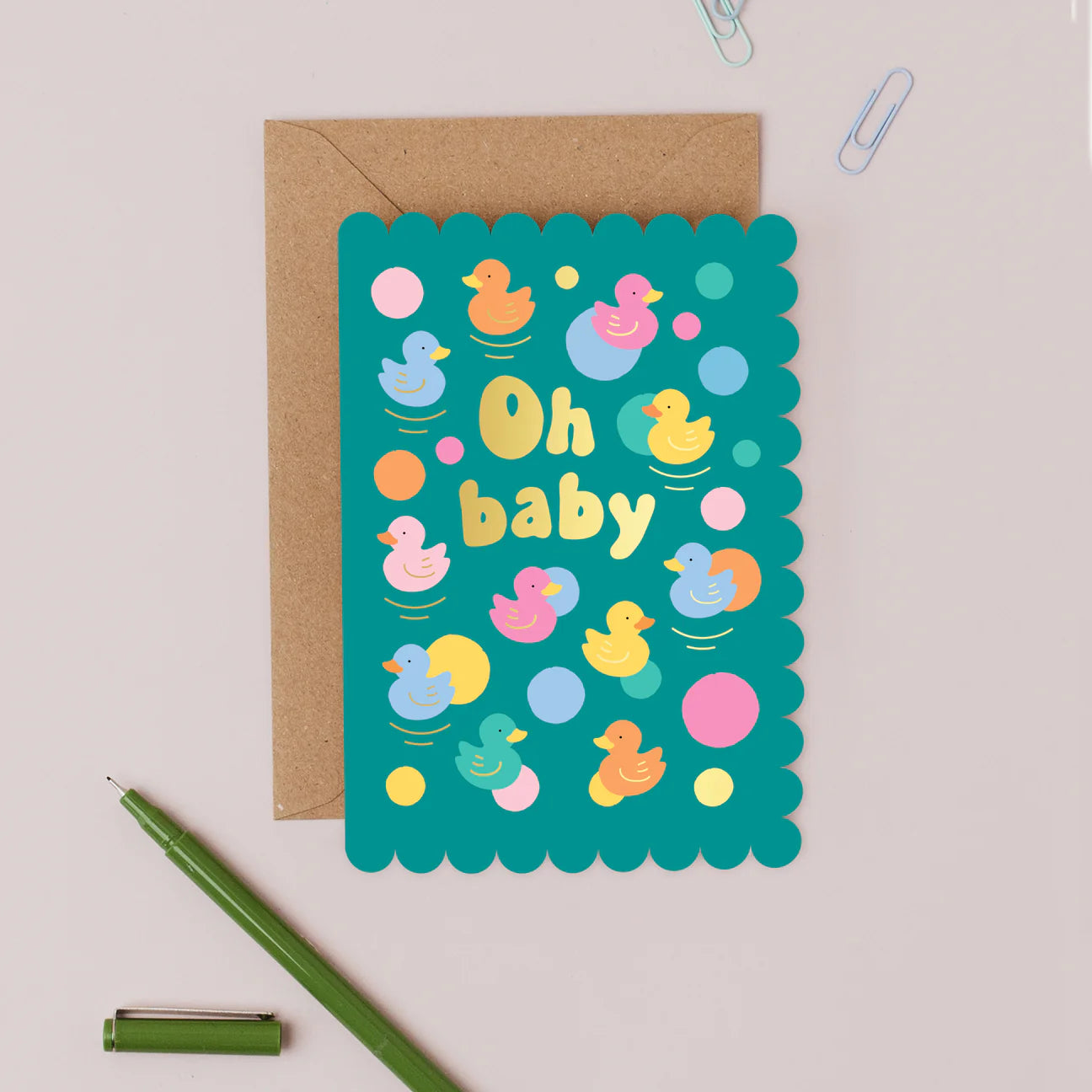 Mifkins greeting card with colourful rubber duck illustrations and 'Oh baby' text, accompanied by a brown envelope on a light background.