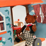Moulin Roty teddy bear in a checkered outfit inside a colourful toy house with floral details.
