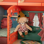 Moulin Roty toy caravan with a teddy bear in a checkered dress and hat inside.