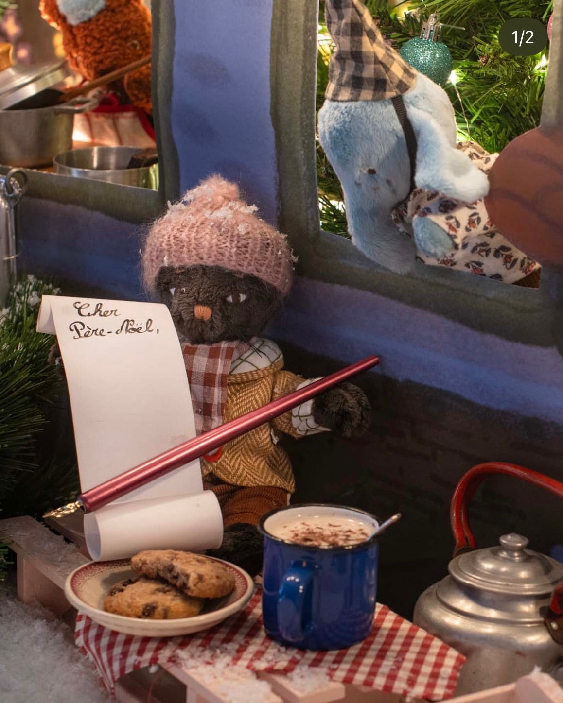 Toy cat in a festive setting with cookies, hot chocolate, and a letter, surrounded by Christmas decorations.