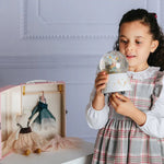 Young girl holding a small glass dome with a toy inside, next to a larger pink box with a toy inside.