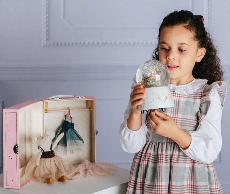 Young girl holding a small glass dome with a toy inside, next to a larger pink box with a toy inside.