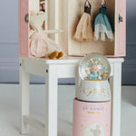 Pink toy wardrobe with dolls and a snow globe on a white surface