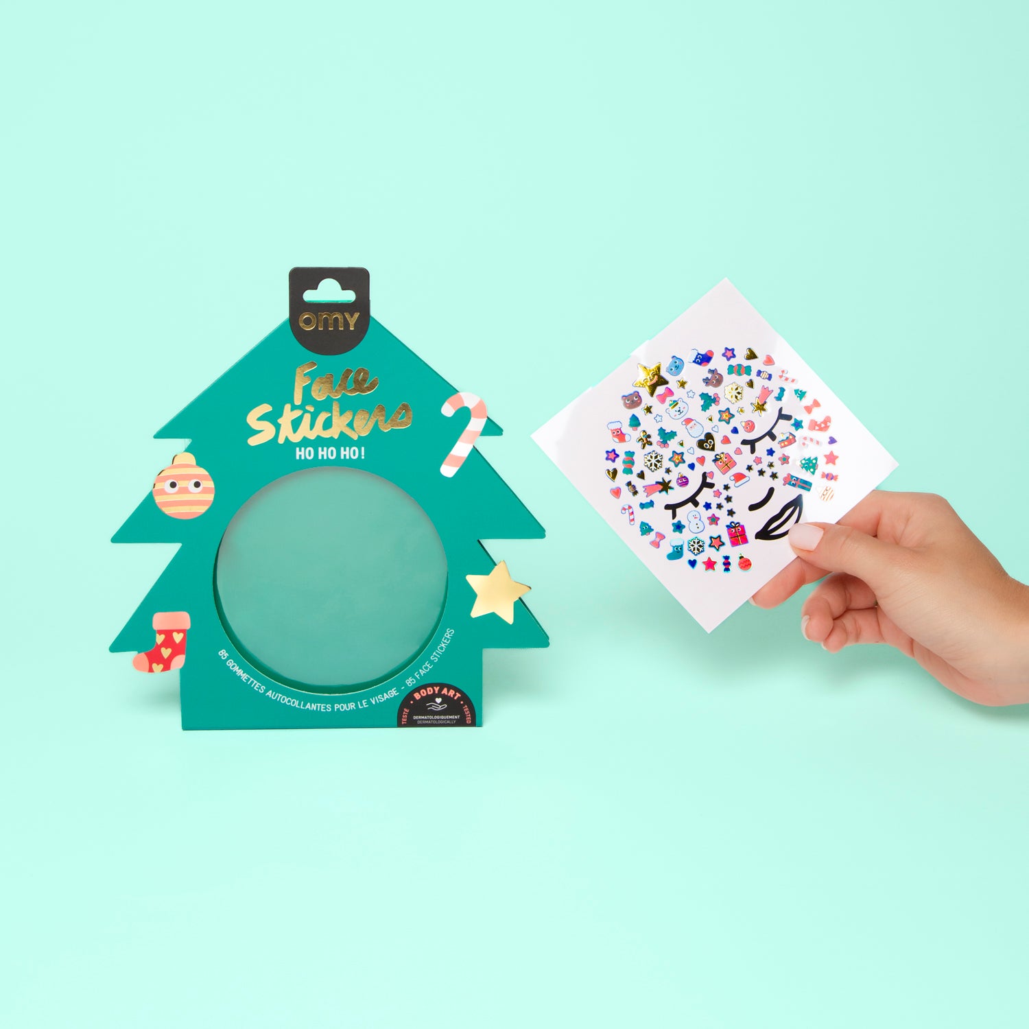 Tree-shaped OMY face sticker set with a hand holding a sheet of stickers against a light green background