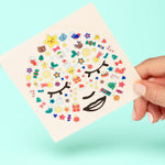 Sheet of colorful OMY face stickers with cartoon designs held by a hand against a light blue background