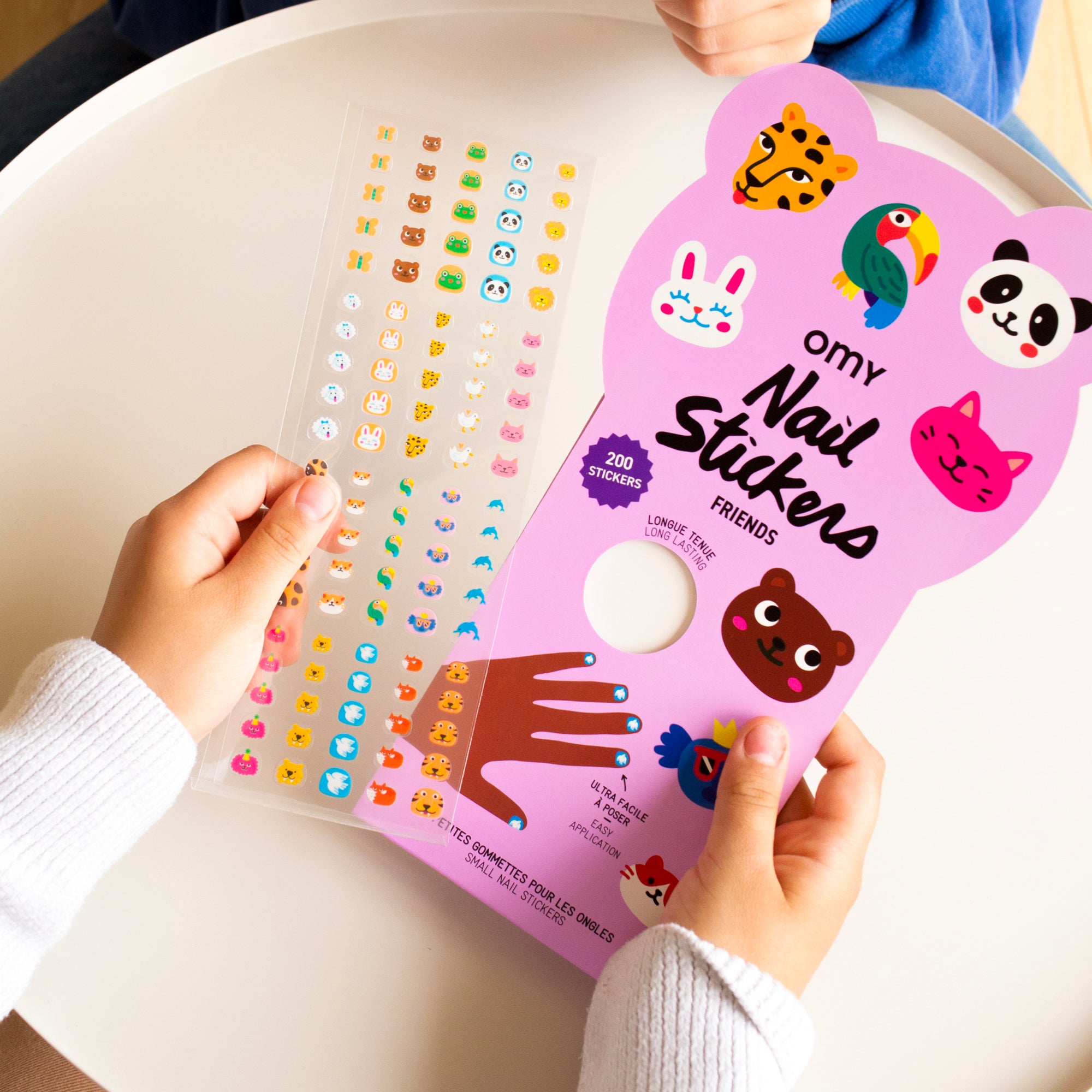 Pink OMY nail sticker sheet with cartoon characters held by a person