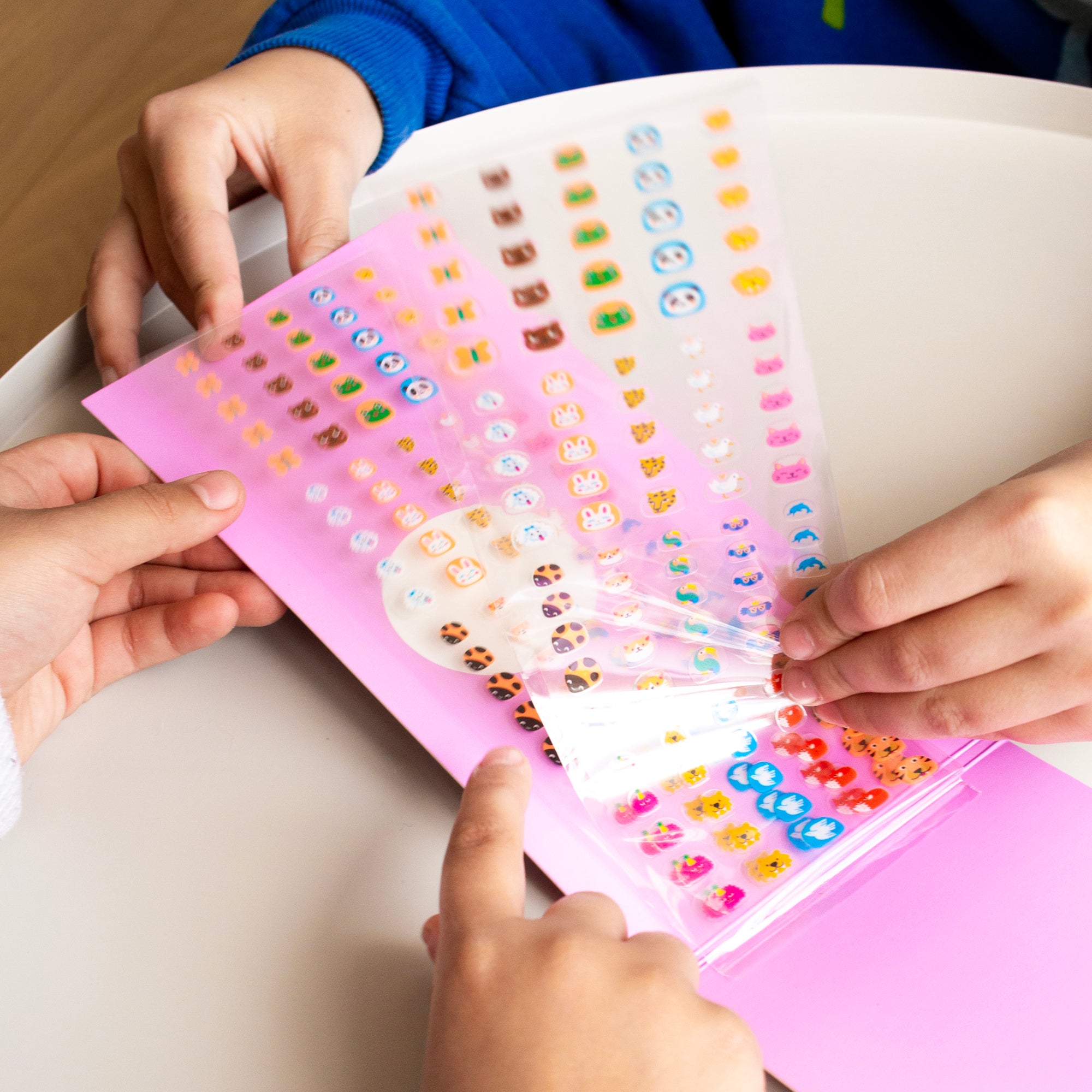 Children's hands opening a pink OMY nail sticker book with colorful stickers.