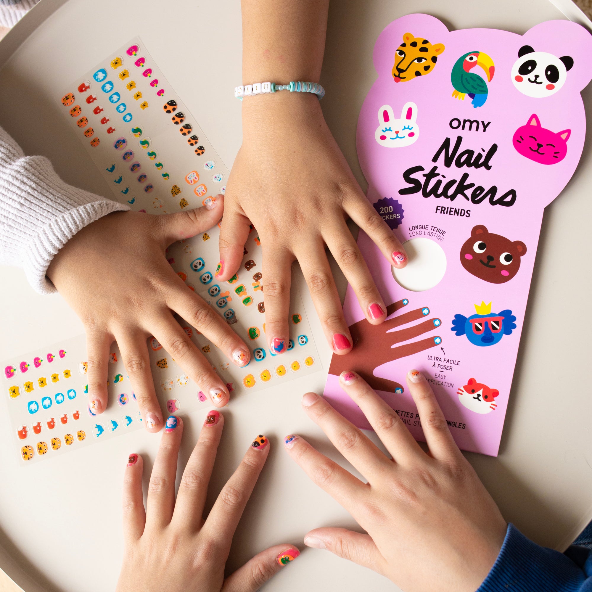 Children's hands with colorful nail stickers applied, next to a pink 'Omy Nail Stickers' pack.