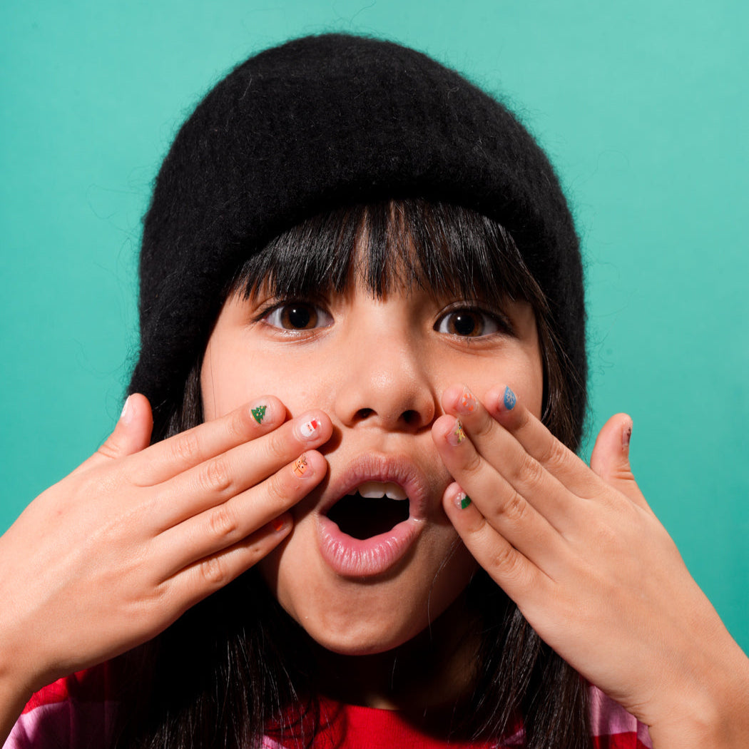 Child with black knit hat covering mouth with hands with OMY nail stickers on teal background