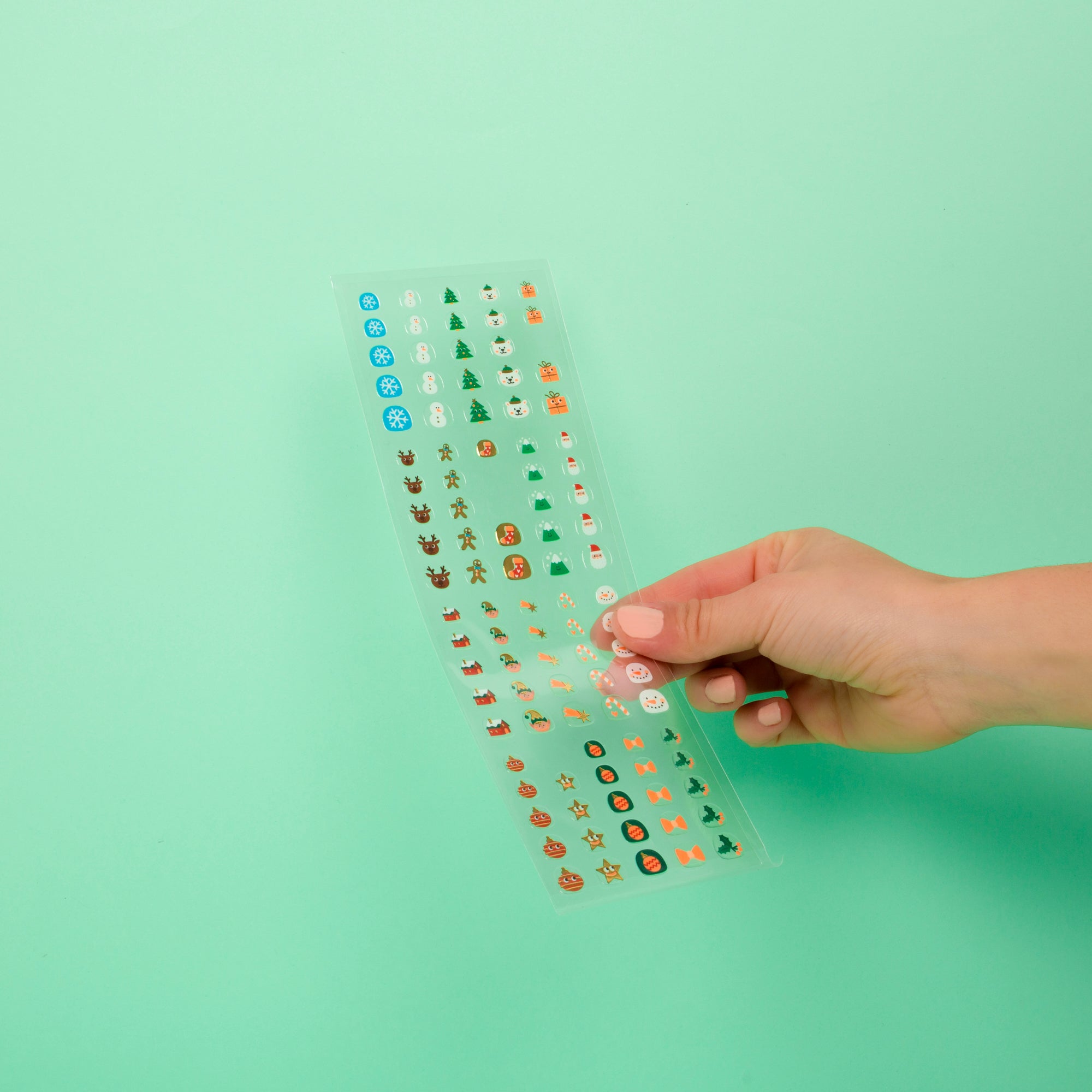 Hand holding a clear sheet with OMY nail stickers against a light green background