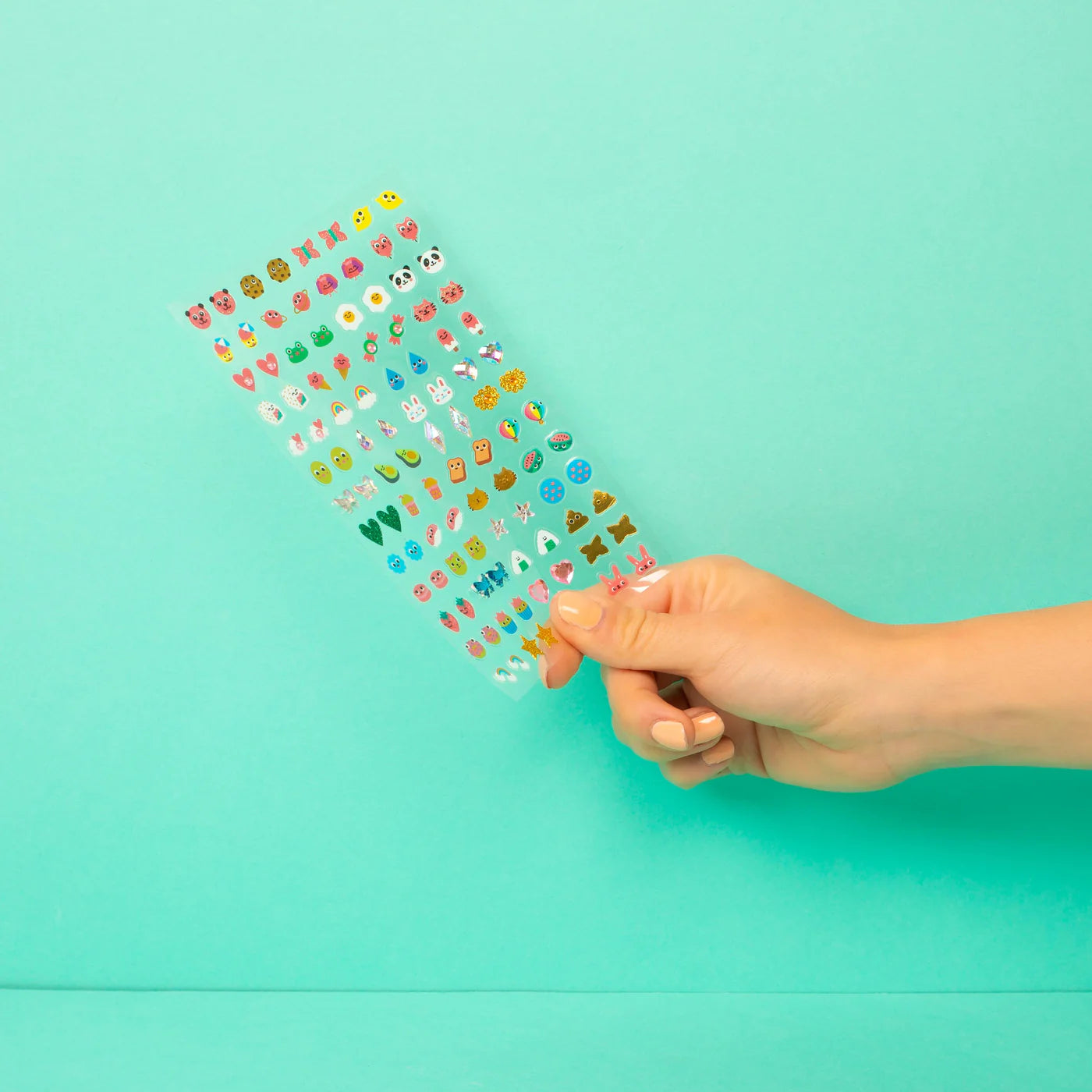 Hand holding a sheet of colorful OMY nail stickers against a turquoise background
