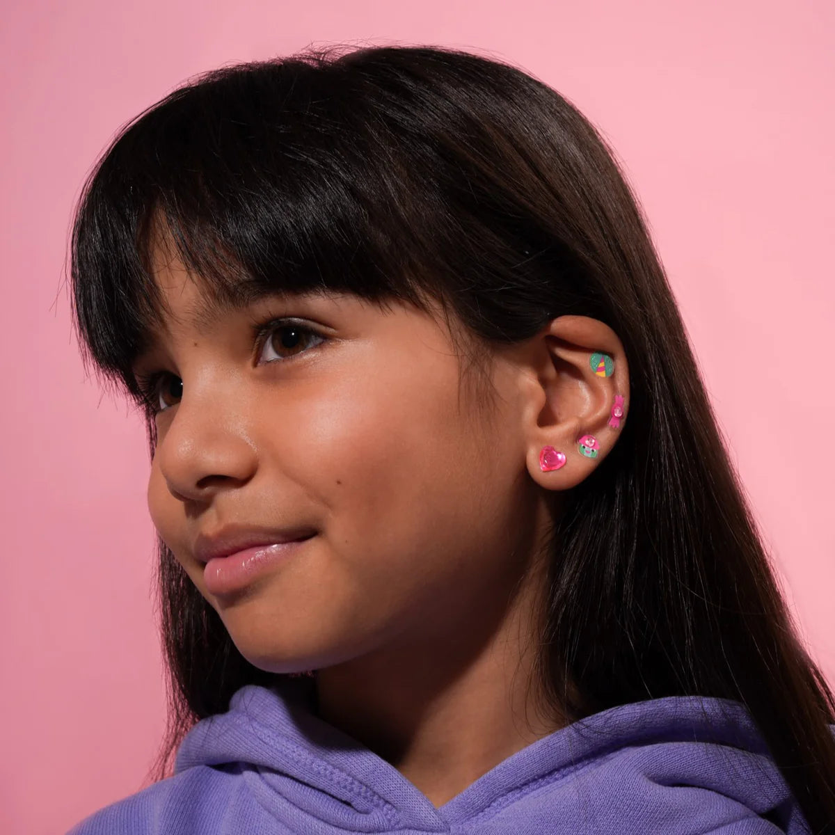 Young girl wearing colorful OMY earrings against a pink background
