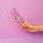 Hand holding OMY colorful nail stickers against a pink background