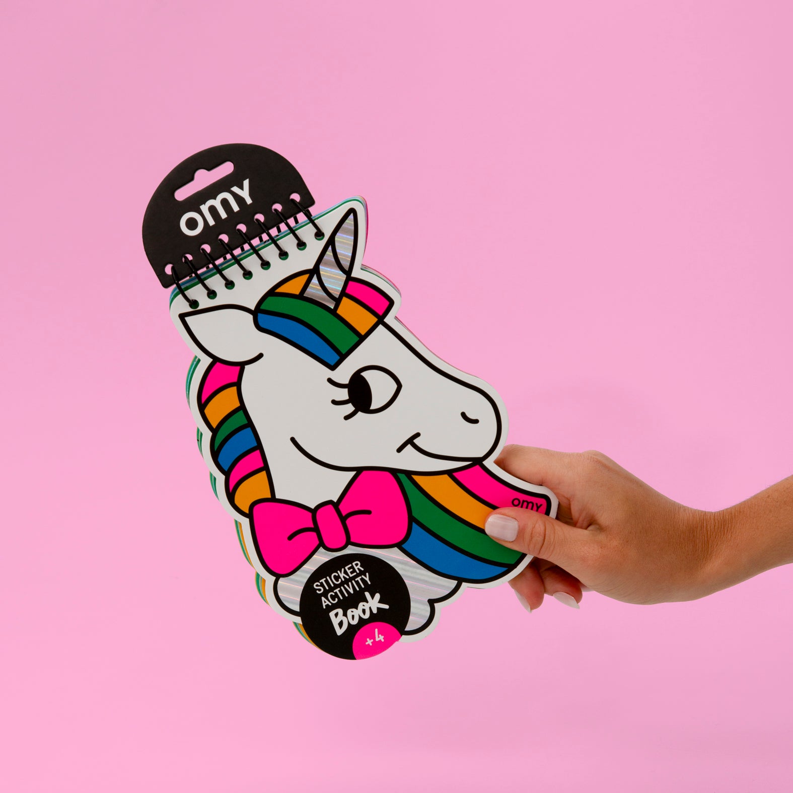 Unicorn-shaped OMY sticker activity book held by a hand against a pink background