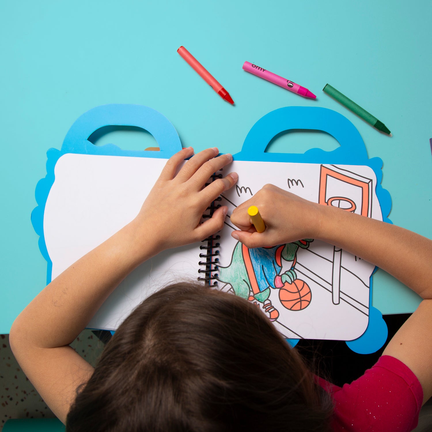 Child coloring an OMY picture with crayons on a blue table