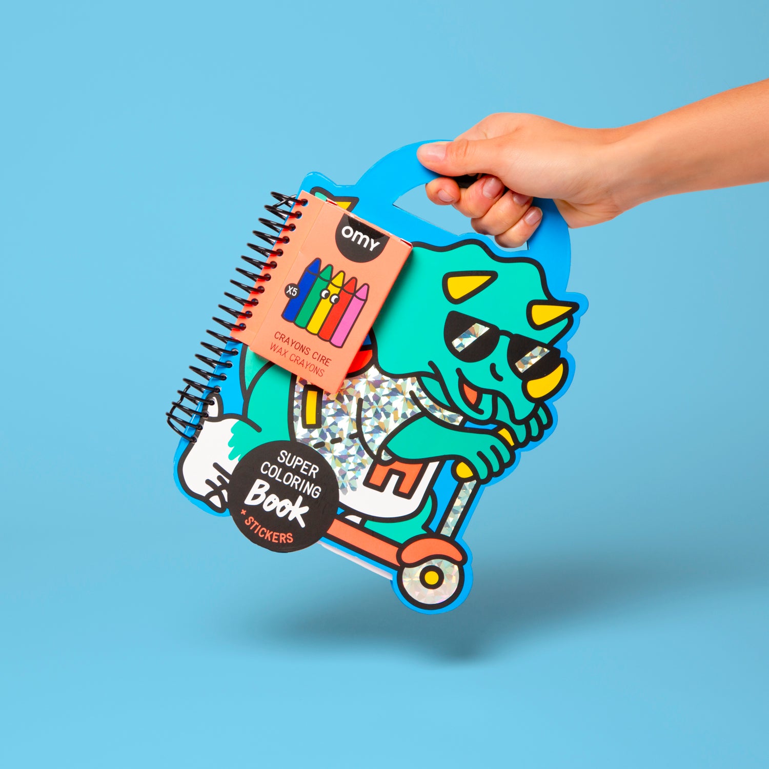 Hand holding a colorful OMY children's activity book with stickers on a blue background