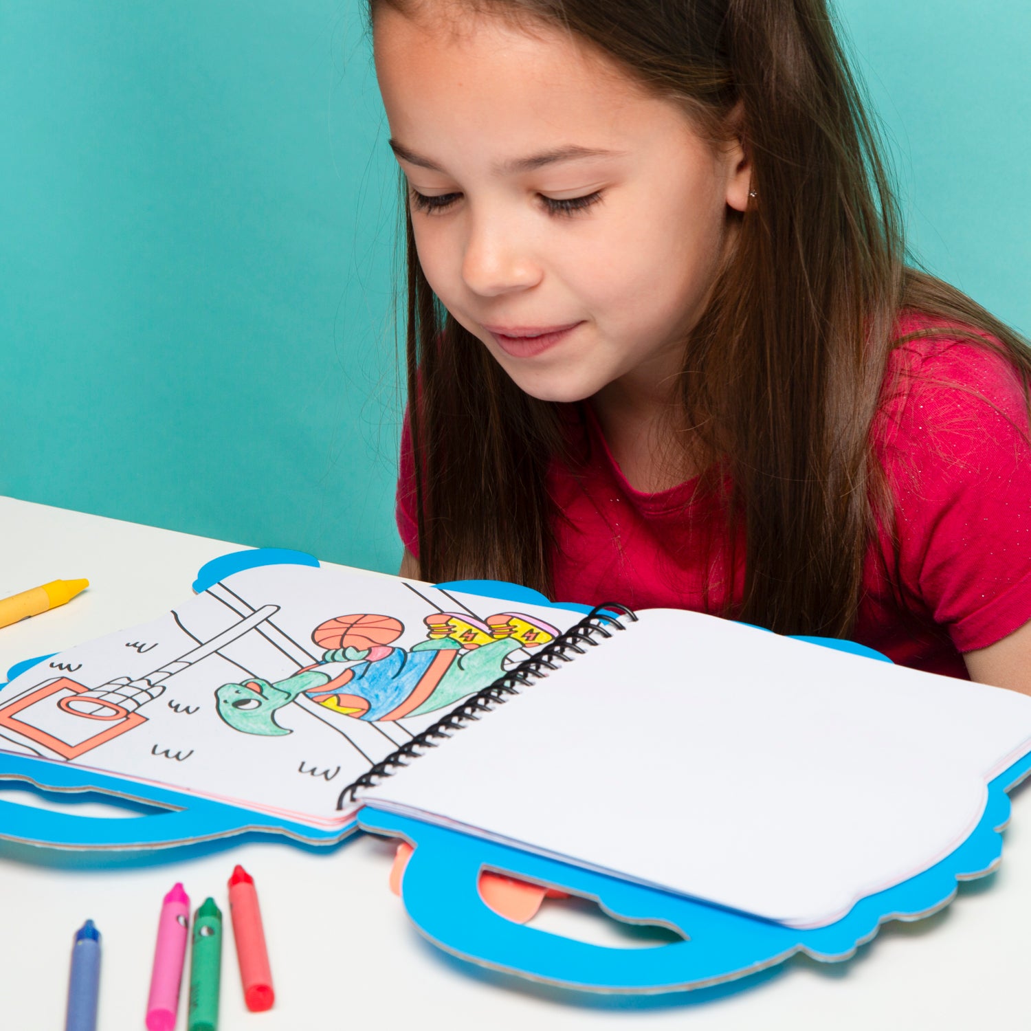 Young girl coloring in an OMY book with crayons on a light blue background