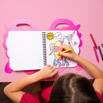 Child coloring a unicorn on a pink table with OMY coloring book and markers.