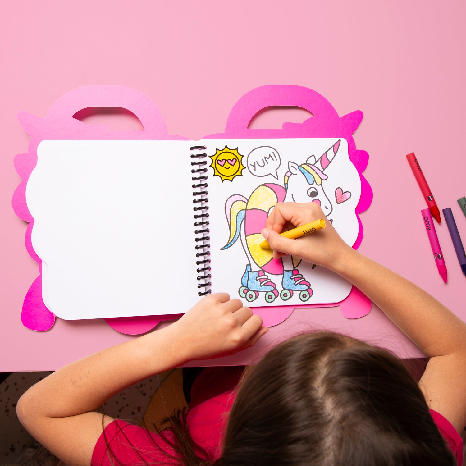 Child coloring a unicorn on a pink table with OMY coloring book and markers.