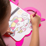 OMY child coloring a unicorn with pink crayon on a pink heart-shaped stand.