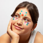 Girl with colorful OMY stickers on her face against a plain background