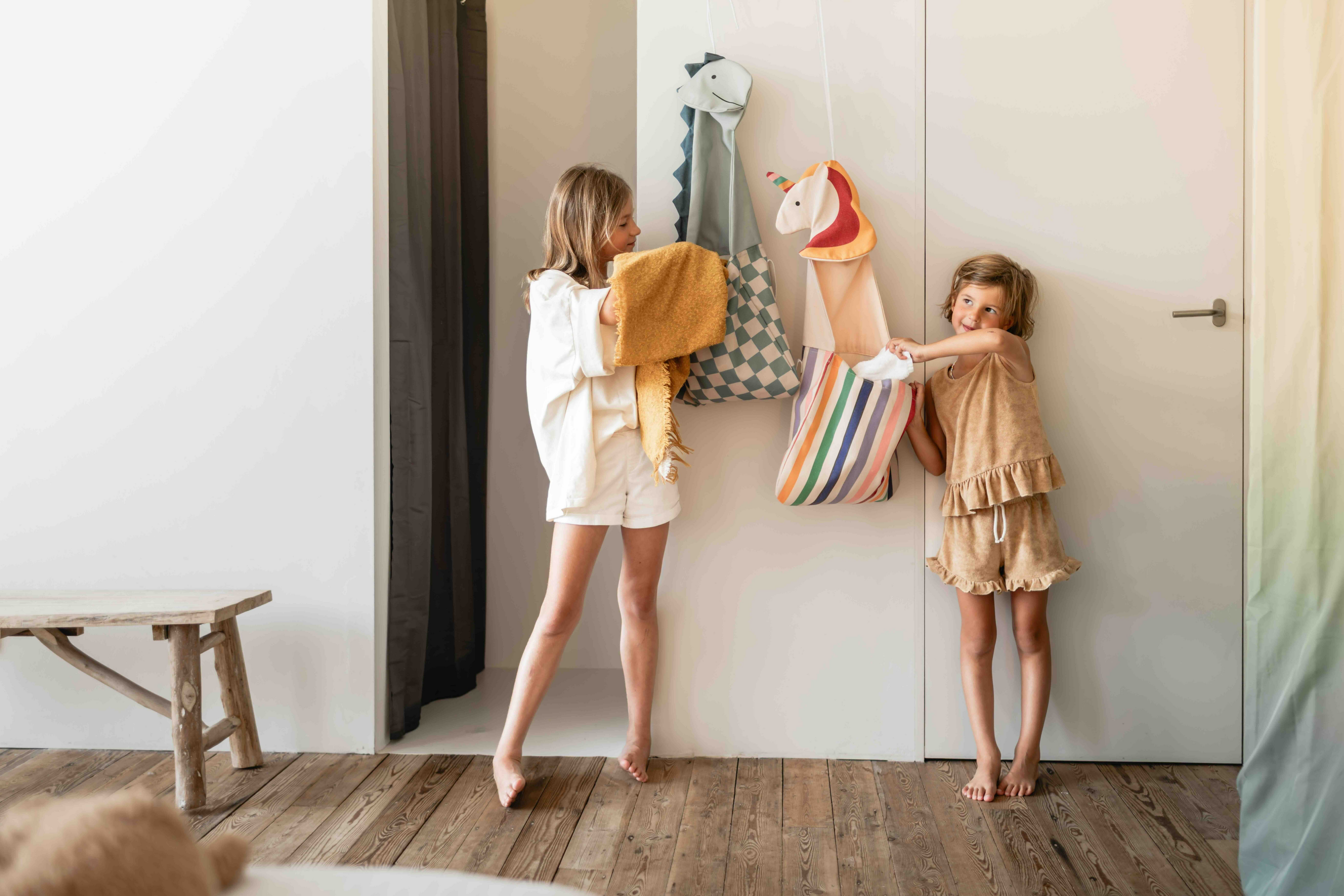 Two children standing in a room with toys on a shelf.