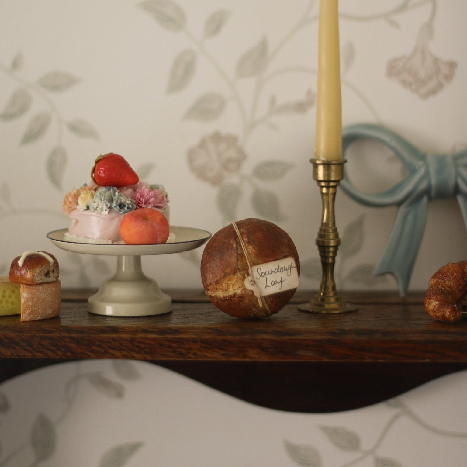 Decorative items including a candle, small cake, and football on a table with floral wallpaper.